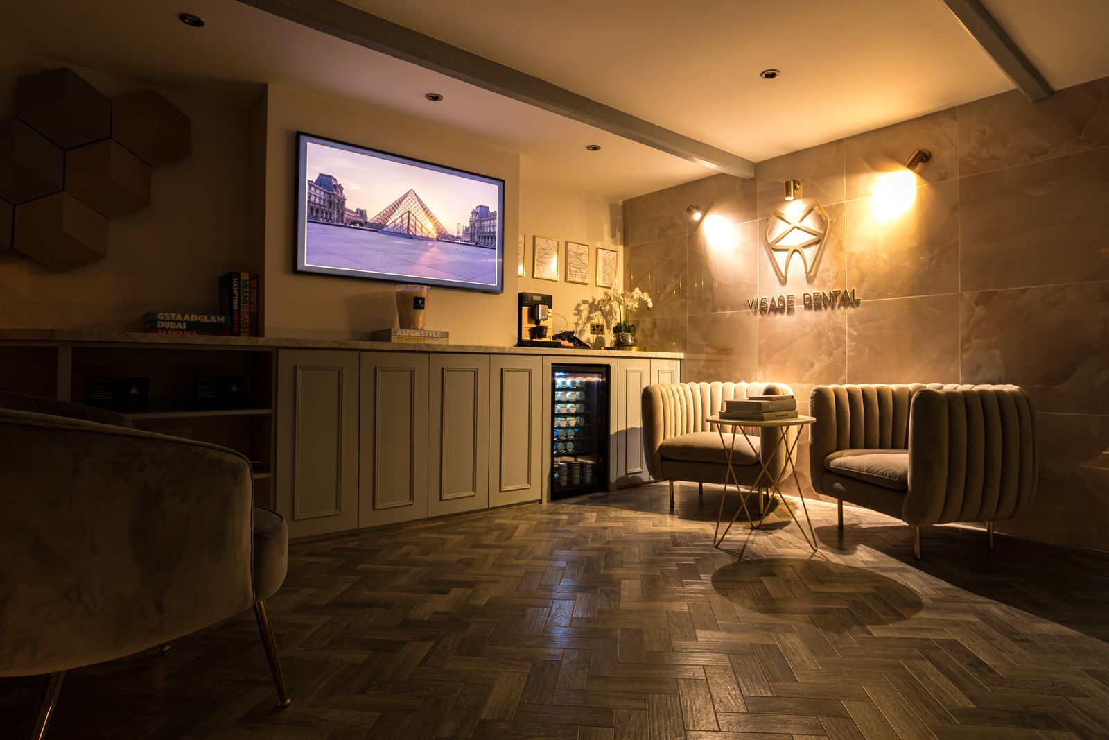Reception at Visage Dental Prestbury with herringbone floor, velvet chairs and the Visage Dental logo wall