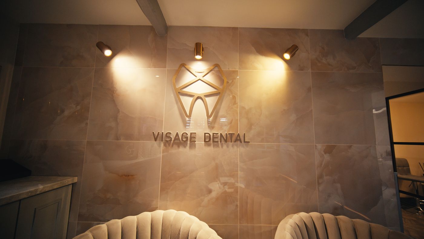 The gold Visage Dental logo on the marble reception wall